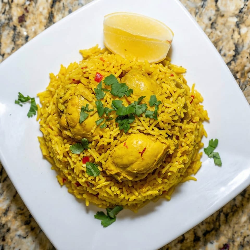Yellow chicken biryani with cilantro and a lemon wedge on a white plate.