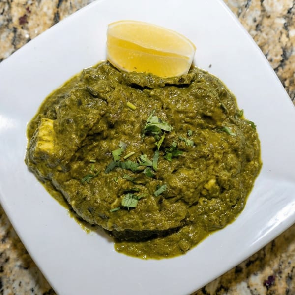 Palak Paneer, a vibrant green spinach and cheese curry, garnished with cilantro and a lemon wedge.
