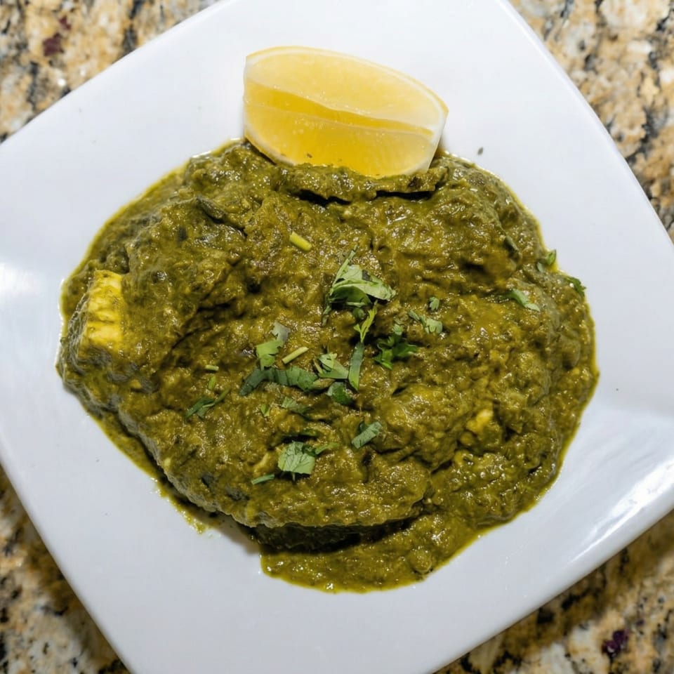 Palak Paneer, a vibrant green spinach and cheese curry, garnished with cilantro and a lemon wedge.